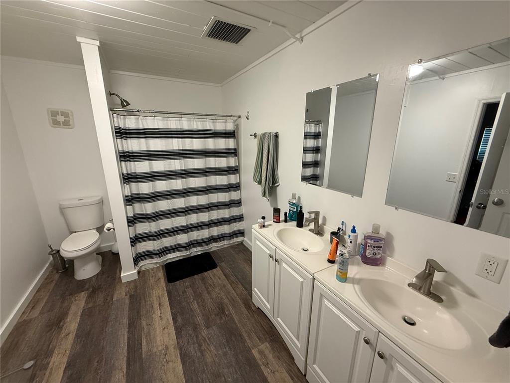 A bathroom features a double vanity, a shower with a striped curtain, and wood-look flooring — 1530 NW 6TH AVENUE, GAINESVILLE, FL