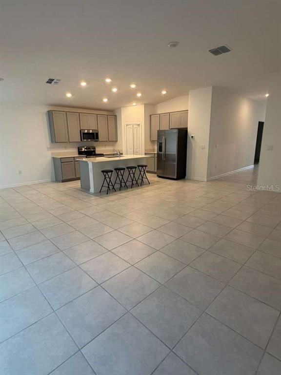 An open-concept kitchen features gray cabinets, stainless steel appliances, and a central island with stools — 2350 BURNEY FALLS LANE, DAVENPORT, FL