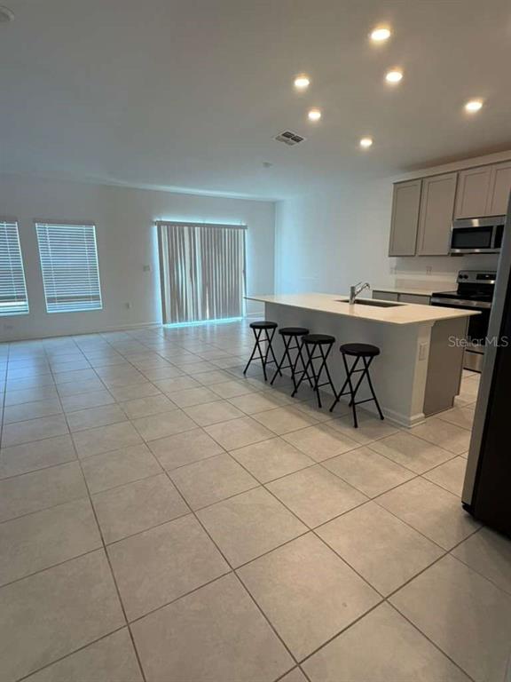An open-concept kitchen features a large island with bar stools and light-colored tile flooring — 2350 BURNEY FALLS LANE, DAVENPORT, FL