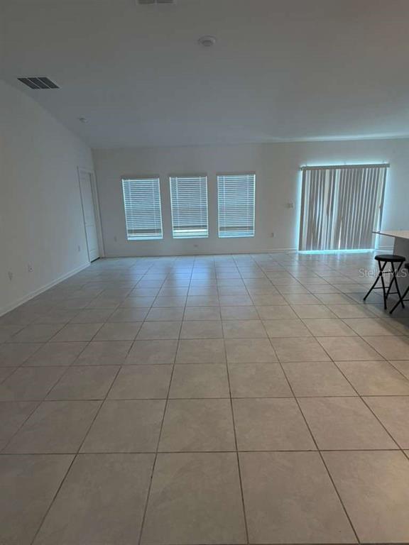 An empty room features light-colored tile flooring, three windows with blinds, and sliding glass doors — 2350 BURNEY FALLS LANE, DAVENPORT, FL