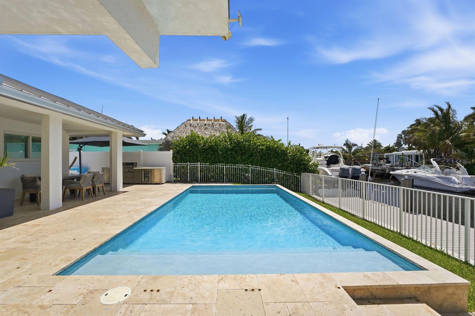 A rectangular swimming pool sits on a stone patio next to a canal with boats — 120 SE 12th Court, Pompano Beach FL 33060, POMPANO BEACH, FL