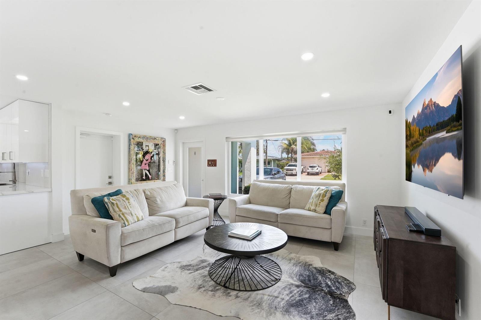 A living room with two beige sofas, a round coffee table, and a wall-mounted television — 120 SE 12th Court, Pompano Beach FL 33060, POMPANO BEACH, FL
