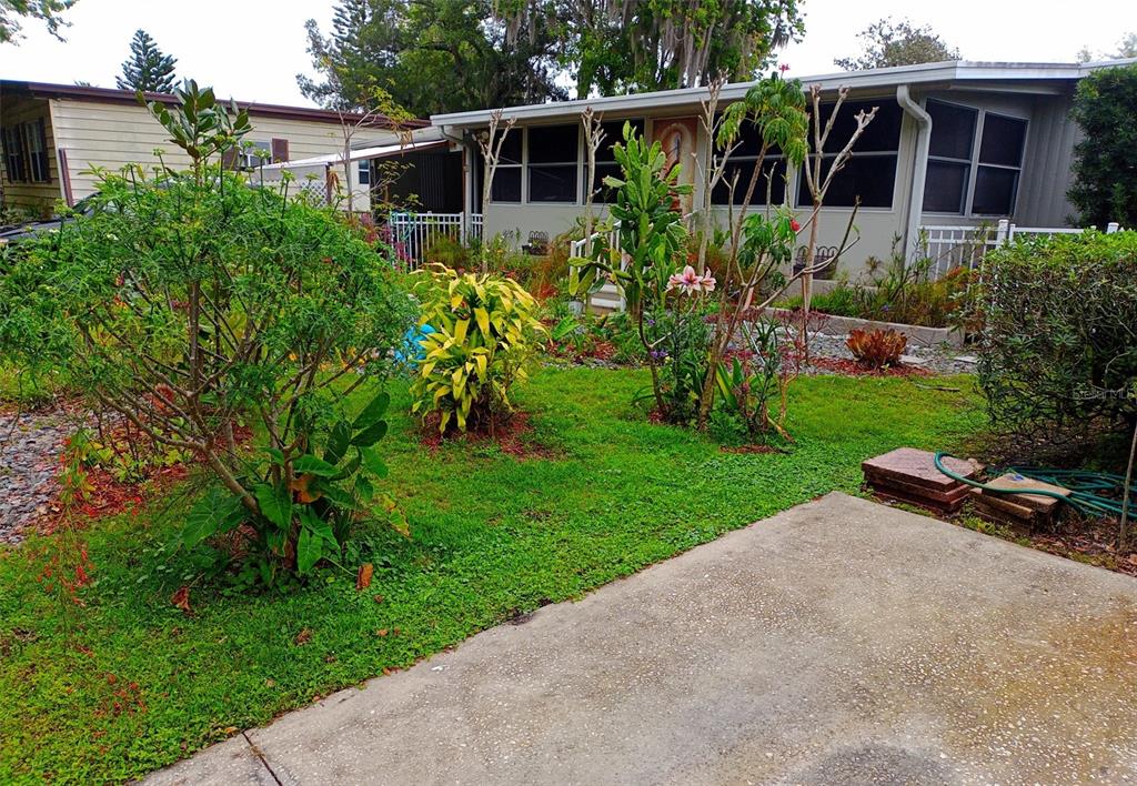 A concrete walkway leads through a lush garden with various plants and flowers toward a street — 109 FERN DRIVE, DEBARY, FL