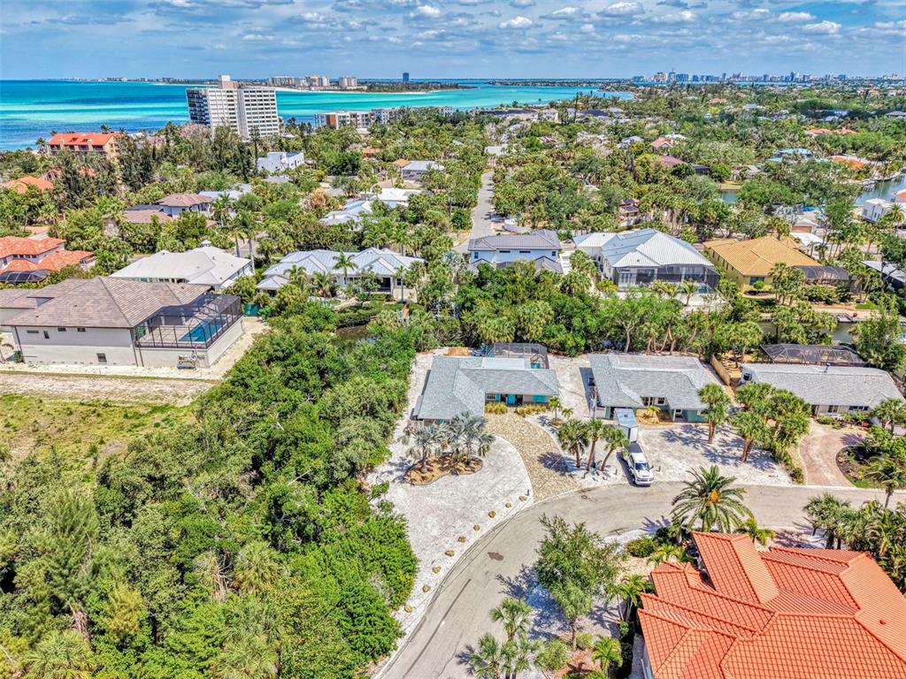 An aerial view shows a residential neighborhood with houses, lush trees, and a coastal bay — 307 AVENIDA DE PARADISIO, SARASOTA, FL