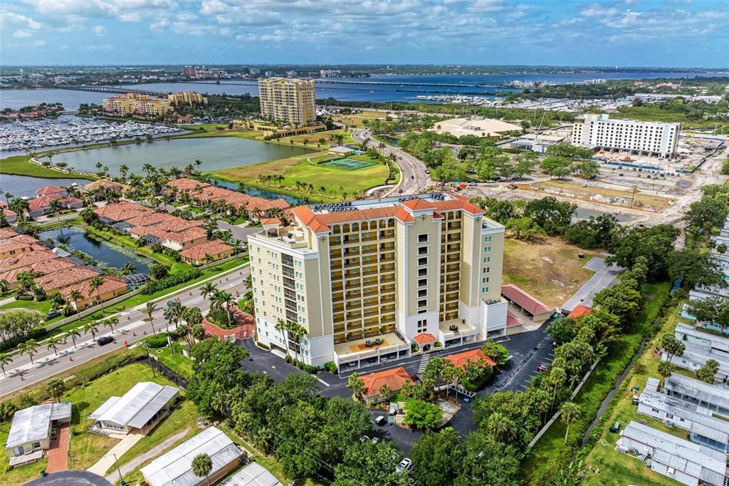 An aerial view shows a tall residential building surrounded by parking, landscaping, and nearby water — 501 HABEN BOULEVARD UNIT 505, PALMETTO, FL