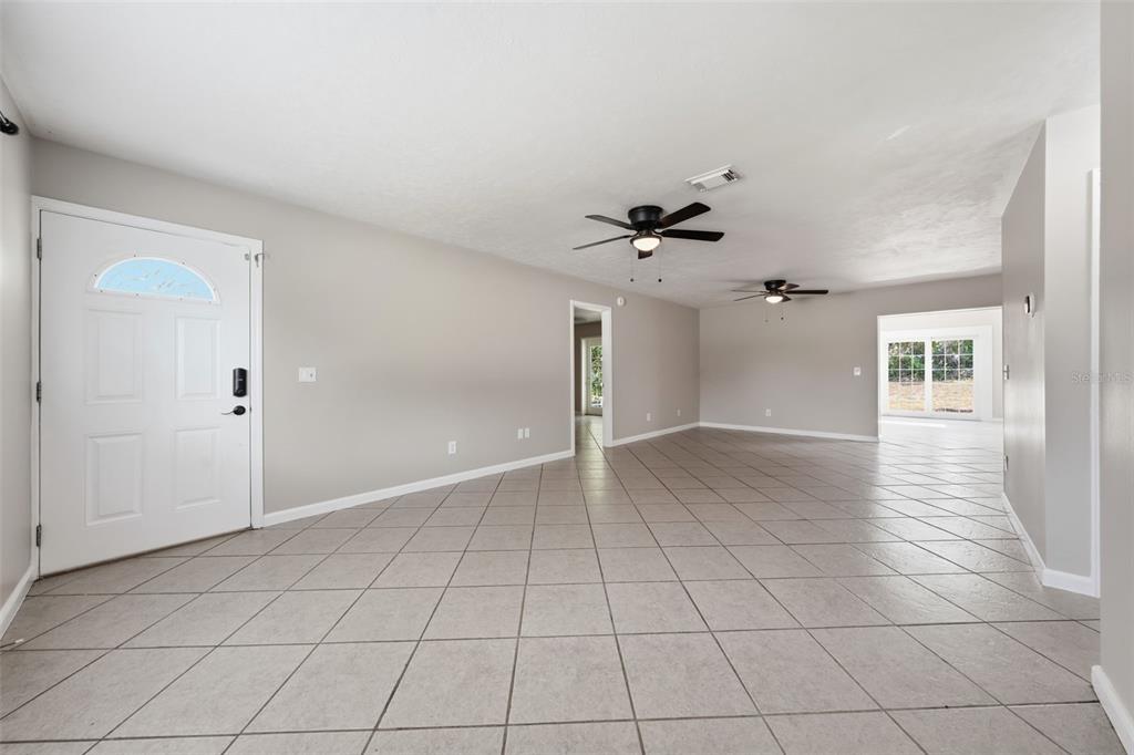 An open-concept living area features light gray walls, neutral tile flooring, and two ceiling fans — 917 ALABAMA WOODS LANE, ORLANDO, FL