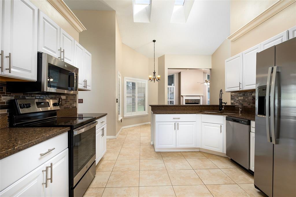 A kitchen with white cabinets, stainless steel appliances, brown granite countertops, and tile flooring — 1058 ALMOND TREE CIRCLE, ORLANDO, FL