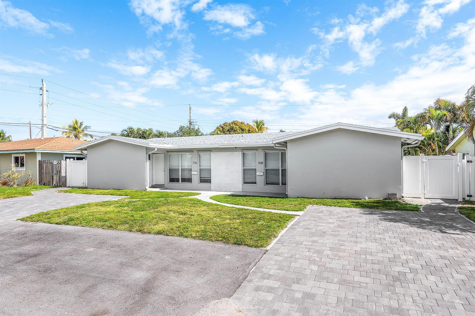 A single-story duplex with gray exterior walls, a paved driveway, and a small front lawn — 708-710 NE 23rd Avenue, Pompano Beach FL 33062, POMPANO BEACH, FL