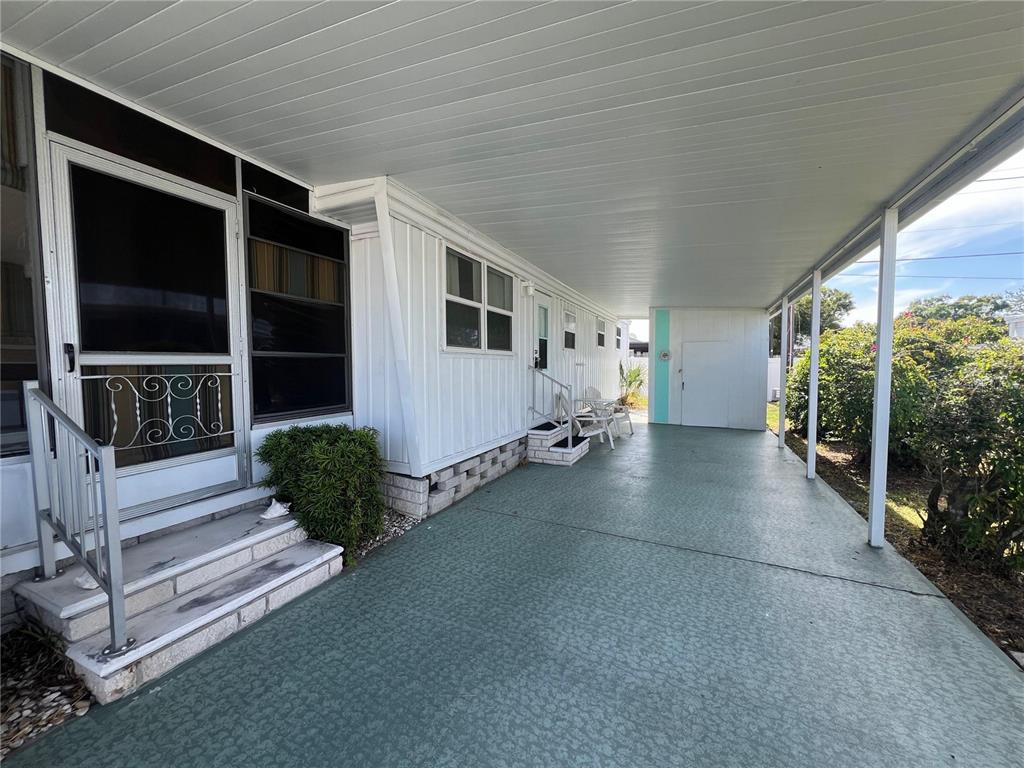 A covered carport with a green textured floor leads to the entrance of a home — 1500 COUNTY ROAD 1 UNIT 95, DUNEDIN, FL