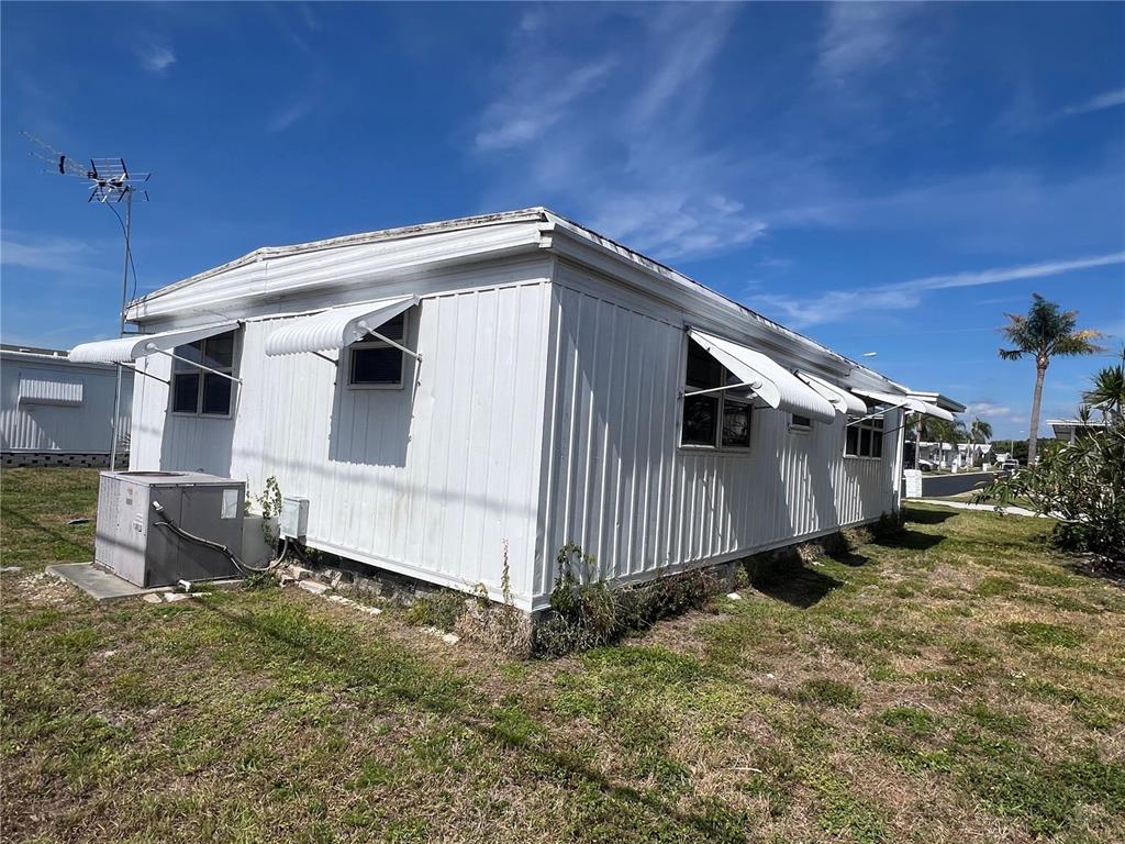 The exterior of a white mobile home features metal siding, window awnings, and an AC unit — 1500 COUNTY ROAD 1 UNIT 95, DUNEDIN, FL