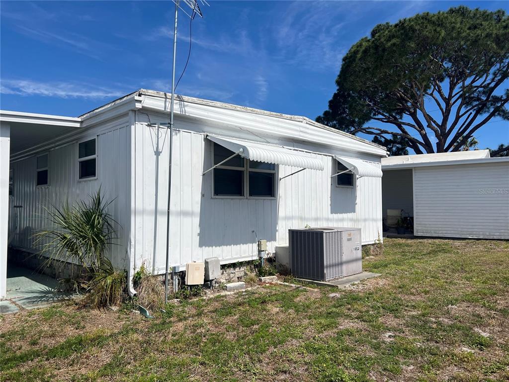 The exterior of a white mobile home features metal siding, window awnings, and an AC unit — 1500 COUNTY ROAD 1 UNIT 95, DUNEDIN, FL
