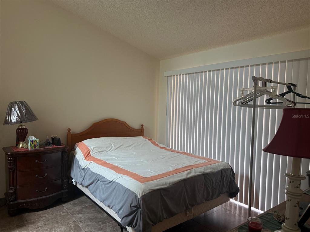 A bedroom features a bed with a wooden headboard, a dresser, and vertical window blinds — 13143 LAVER LANE, ORLANDO, FL