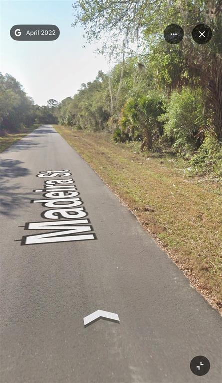 A paved road lined with trees and vegetation stretches into the distance — 1099 MADEIRA STREET, PORT CHARLOTTE, FL