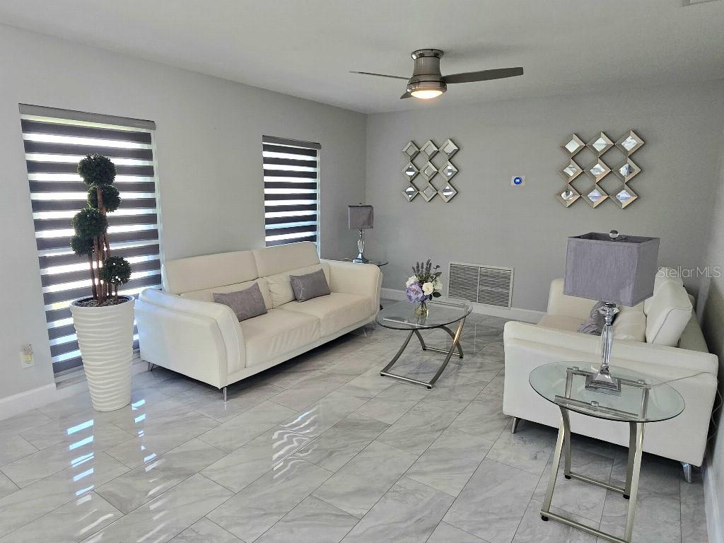 A living room features white sofas, glass tables, gray tile floors, and two decorative wall mirrors — 7002 DANEWOOD COURT, TAMPA, FL