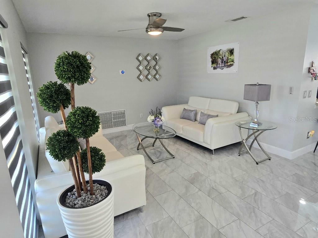 A living room features white sofas, a glass coffee table, and light gray tile flooring — 7002 DANEWOOD COURT, TAMPA, FL