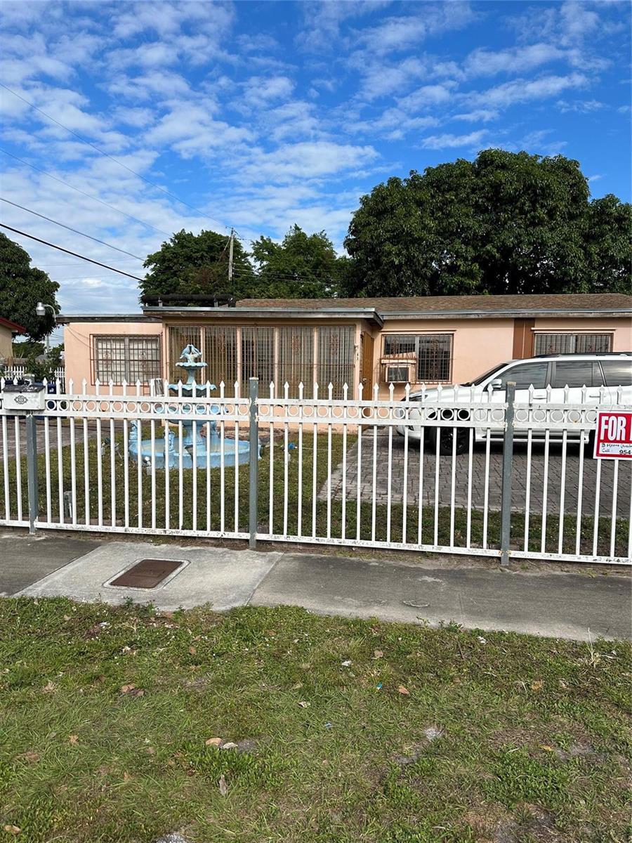 A single-story house with a white metal fence, a front fountain, and a parked SUV — MIAMI GARDENS, FL