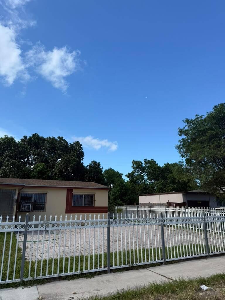 A single-story house with a white metal fence and a gravel yard under a blue sky — MIAMI GARDENS, FL