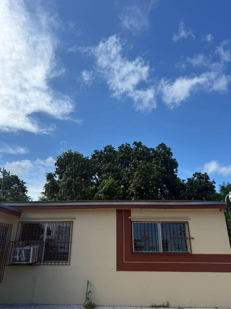 A single-story house with beige walls, brown trim, and window security bars under a blue sky — MIAMI GARDENS, FL