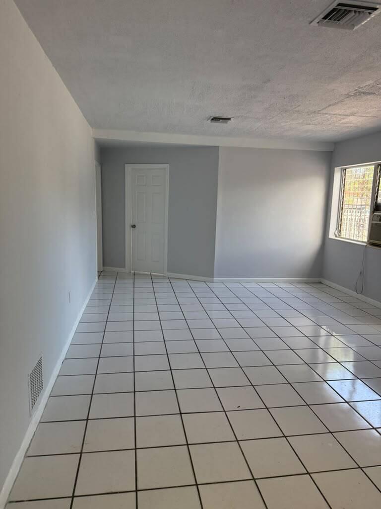 An empty room features white tiled floors, light gray walls, and a single white door — MIAMI GARDENS, FL