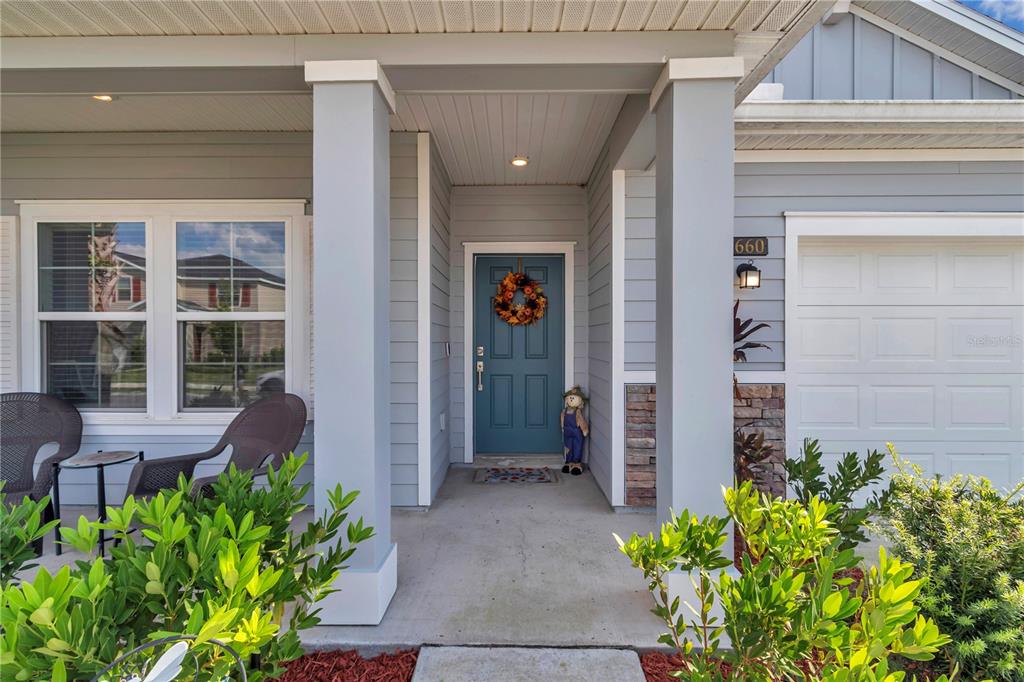 The exterior of a house features a covered porch, a blue front door, and landscaping — 5660 SW 93RD STREET, OCALA, FL