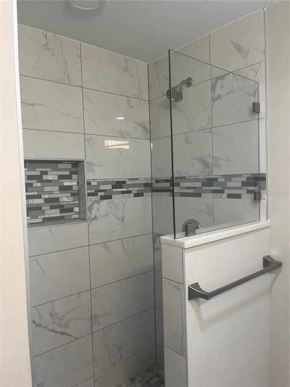 A walk-in shower features white marble-look wall tiles, a decorative mosaic accent strip, and glass — 7320 FREEBERG CIRCLE, PORT CHARLOTTE, FL
