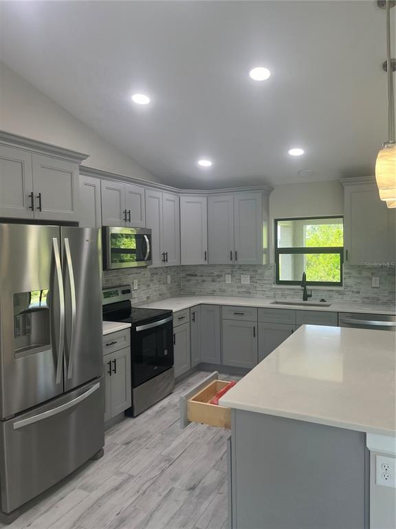 A modern kitchen features gray cabinets, stainless steel appliances, white countertops, and light wood-look flooring — 7320 FREEBERG CIRCLE, PORT CHARLOTTE, FL