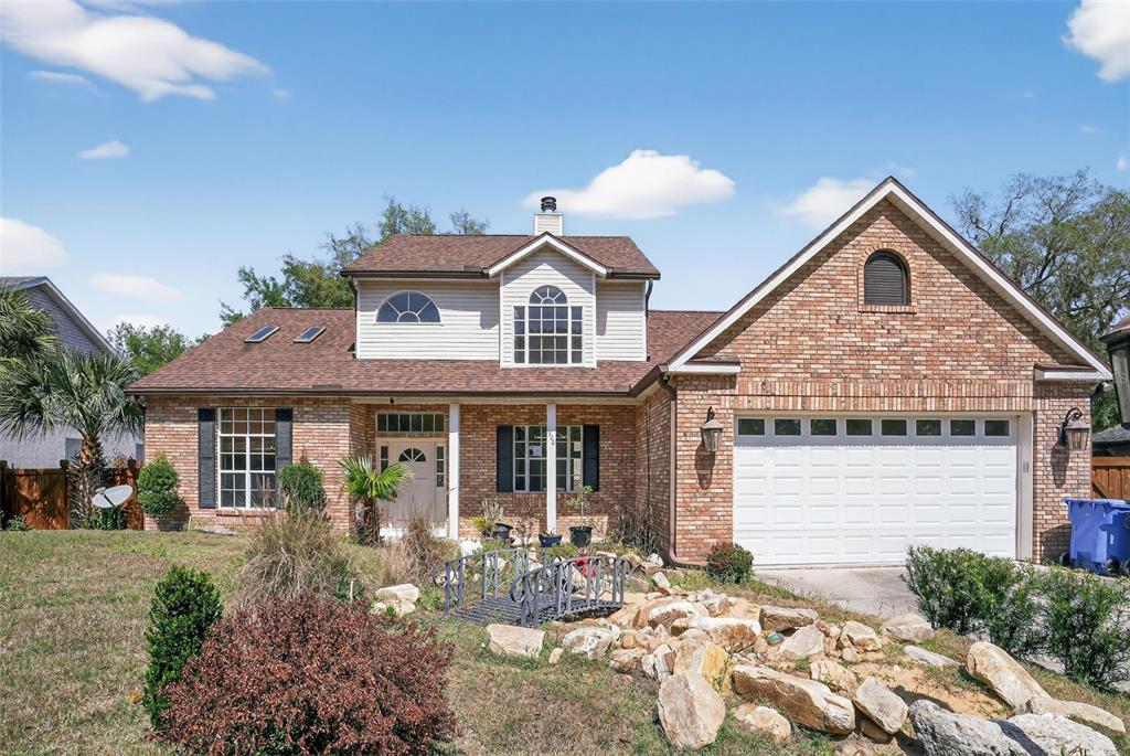 A two-story brick house features a front-facing garage, a small decorative bridge, and landscaping — 902 LINGO COURT, OVIEDO, FL