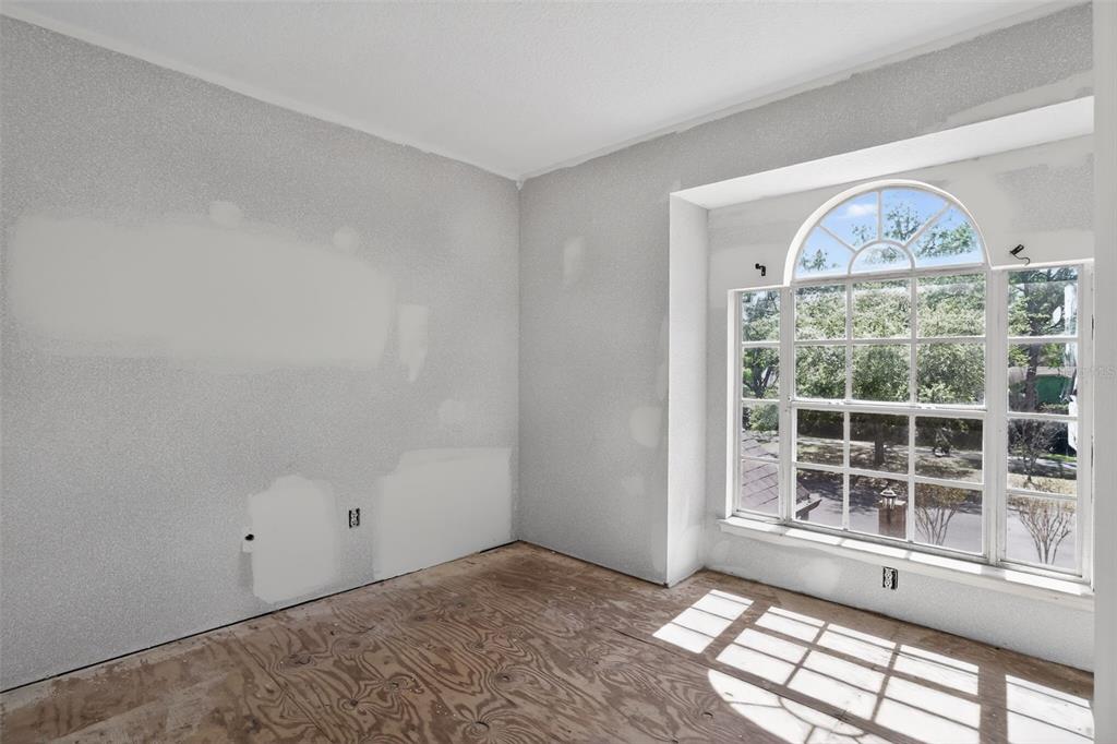 An unfinished room with bare plywood floors, drywall patches, and a large arched window — 902 LINGO COURT, OVIEDO, FL