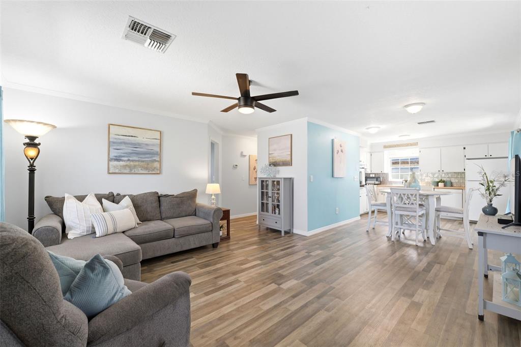 A living room with wood-look flooring, a grey sectional sofa, and an open-concept kitchen — 6129 ELMHURST DRIVE, NEW PORT RICHEY, FL