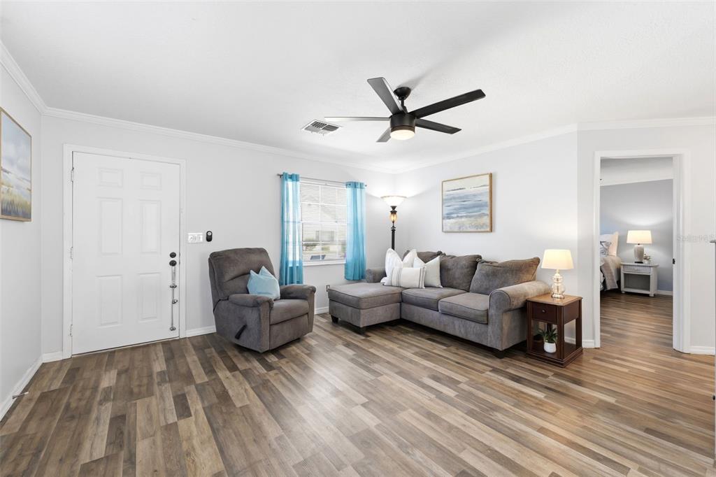 A living room features gray wood-look flooring, a sectional sofa, a recliner, and blue curtains — 6129 ELMHURST DRIVE, NEW PORT RICHEY, FL