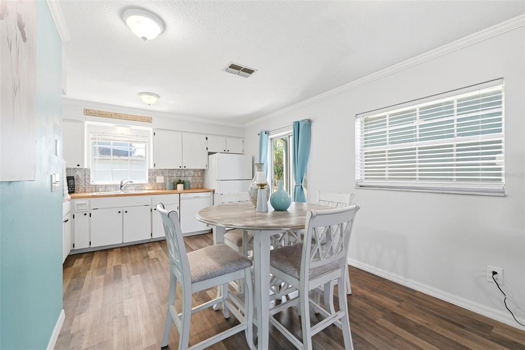 A kitchen and dining area with white cabinets, wood-look flooring, and a round wooden table — 6129 ELMHURST DRIVE, NEW PORT RICHEY, FL