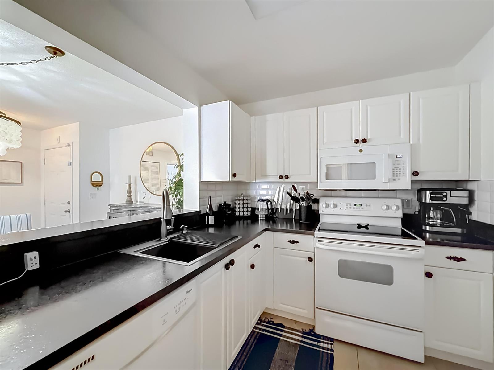 A kitchen features white cabinets, black countertops, a white stove, and a stainless steel sink — 1341 SE 3rd Avenue # 210, Dania Beach FL 33004, DANIA BEACH, FL