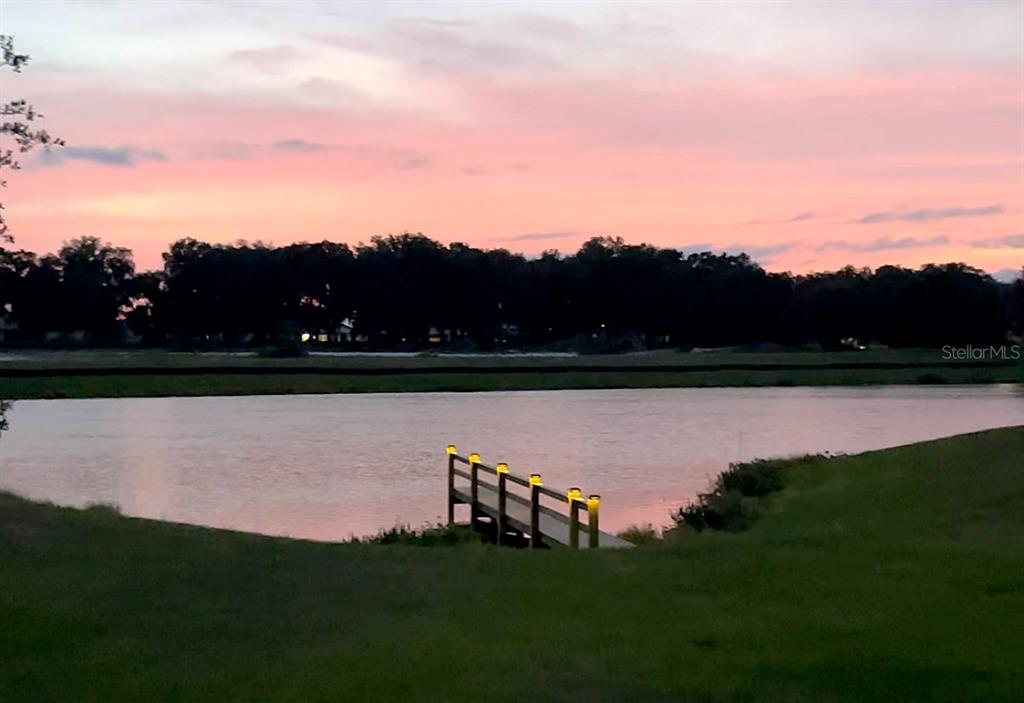 A wooden dock with illuminated posts extends into a lake under a pink sunset sky — 3950 CARRICK BEND DRIVE, KISSIMMEE, FL