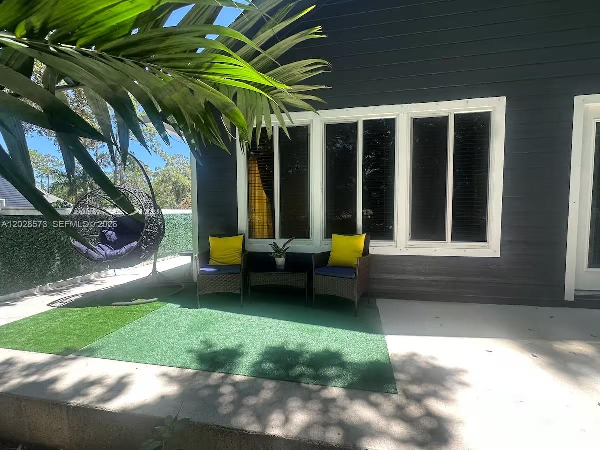 A patio features two wicker chairs with yellow pillows, a small table, and a hanging chair — 12876 N 154th Rd N # A, Jupiter FL 33478, JUPITER, FL