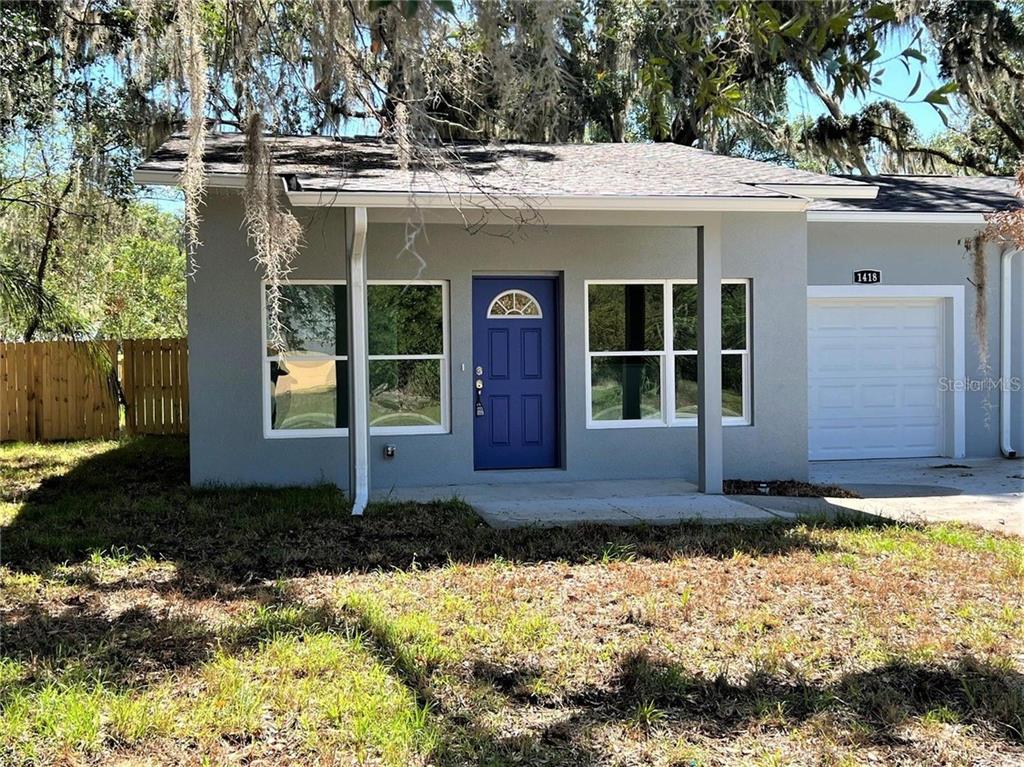 A single-story gray house features a blue front door, a covered porch, and a garage — 1418 N ORANGE STREET, MOUNT DORA, FL