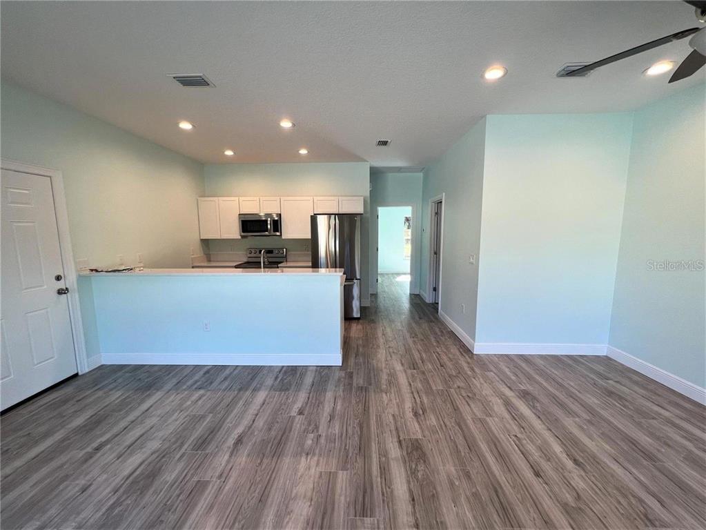 A kitchen with white cabinets and stainless steel appliances overlooks a living area with wood-look flooring — 1418 N ORANGE STREET, MOUNT DORA, FL