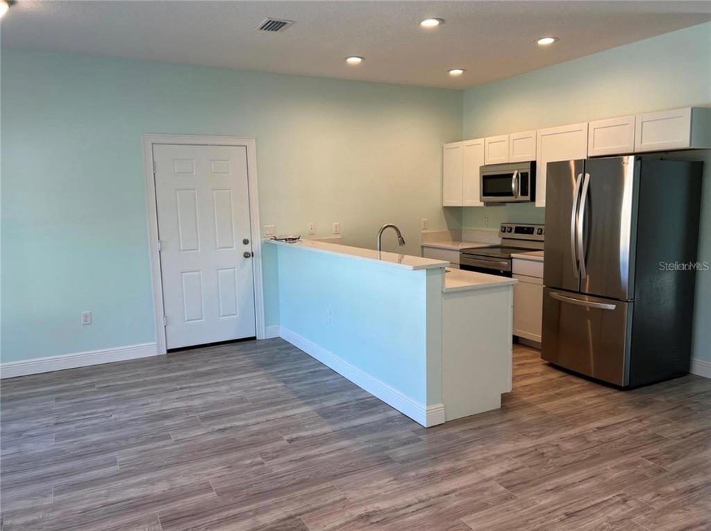 A kitchen features white cabinets, stainless steel appliances, and a breakfast bar with light flooring — 1418 N ORANGE STREET, MOUNT DORA, FL