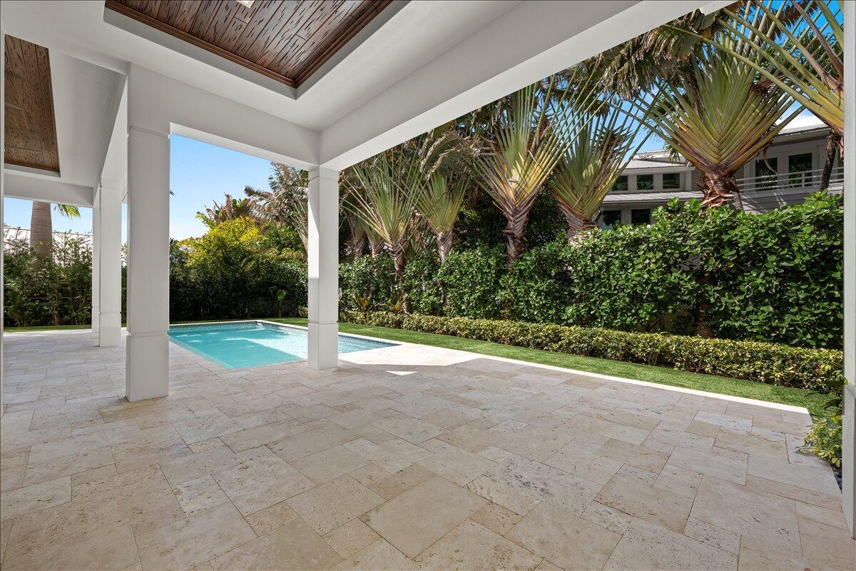 A covered stone patio overlooks a swimming pool and a lushly landscaped backyard — 187 Shelter Lane, Jupiter FL 33469, JUPITER, FL