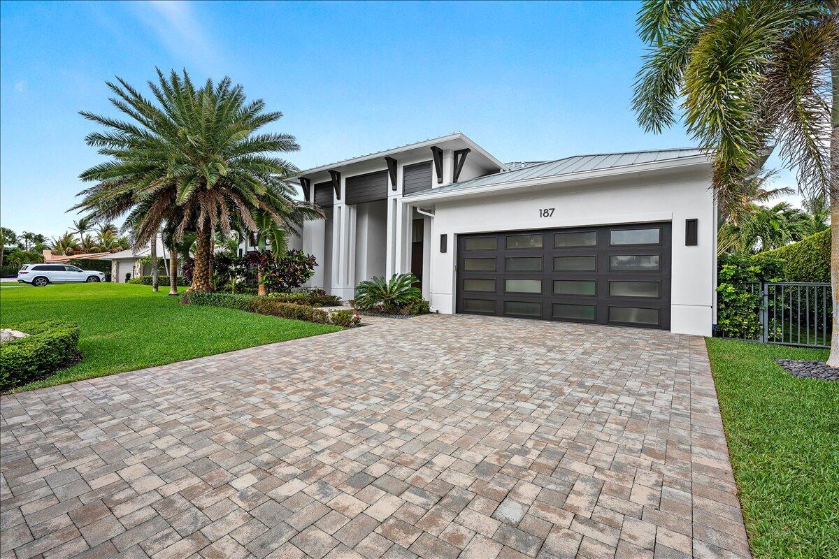 A modern single-story house with a paved driveway, a multi-panel garage door, and palm trees — 187 Shelter Lane, Jupiter FL 33469, JUPITER, FL
