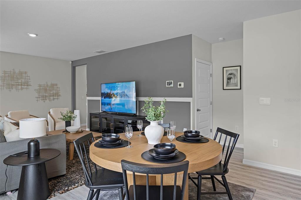 A dining area with a round wooden table and black chairs sits before a living room — 4011 LIMEKLIN FALLS LOOP, DAVENPORT, FL