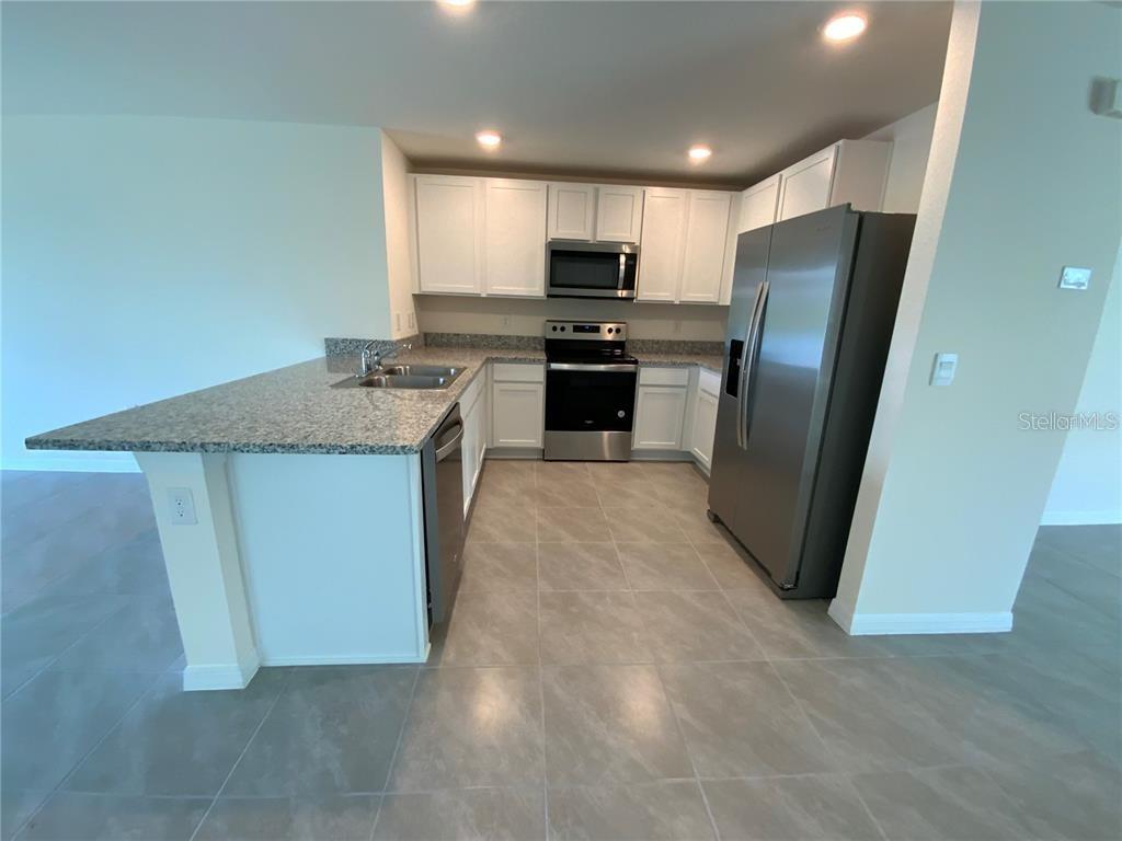 A kitchen features white cabinets, granite countertops, stainless steel appliances, and light tile flooring — 4603 SAND DOLLAR WAY, ZEPHYRHILLS, FL