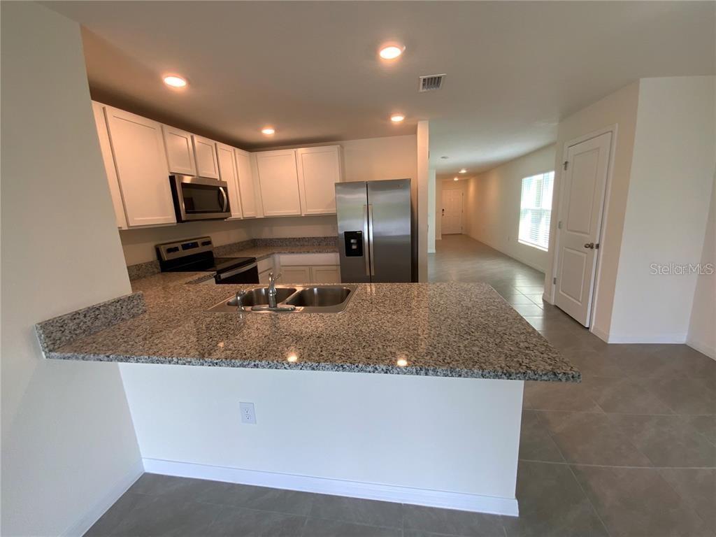 A kitchen features white cabinets, granite countertops, stainless steel appliances, and tile flooring — 4603 SAND DOLLAR WAY, ZEPHYRHILLS, FL