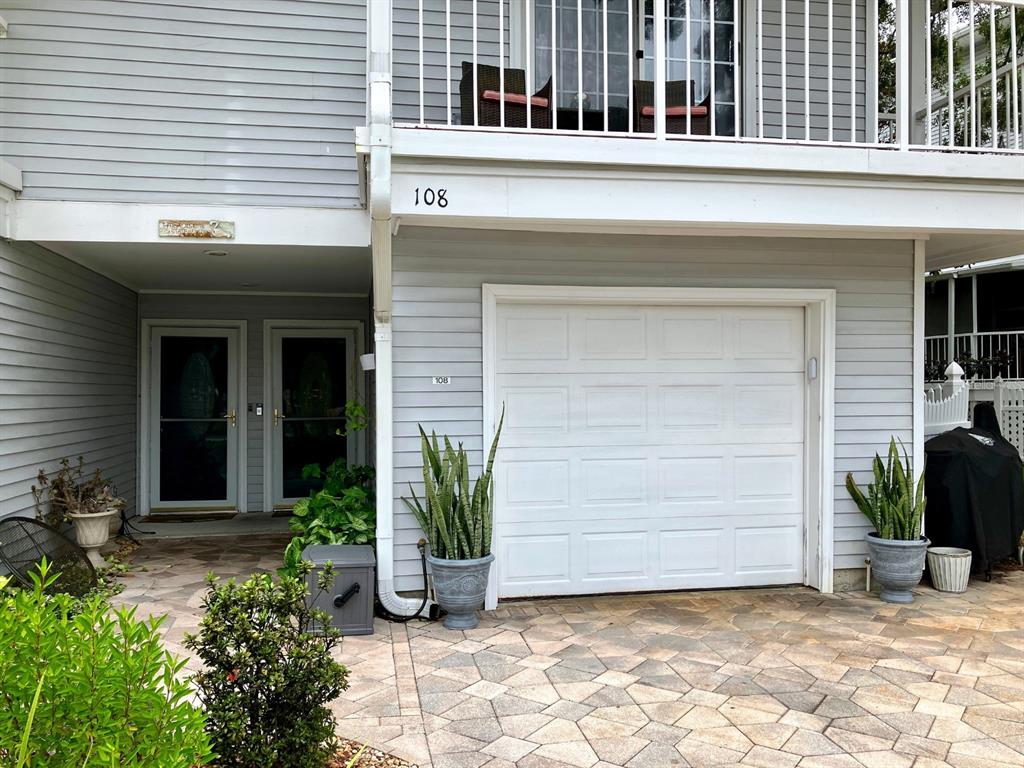 A light gray house exterior features a white garage door, two entry doors, and potted plants — 2015 VISTA DEL SOL CIRCLE UNIT 108, LUTZ, FL