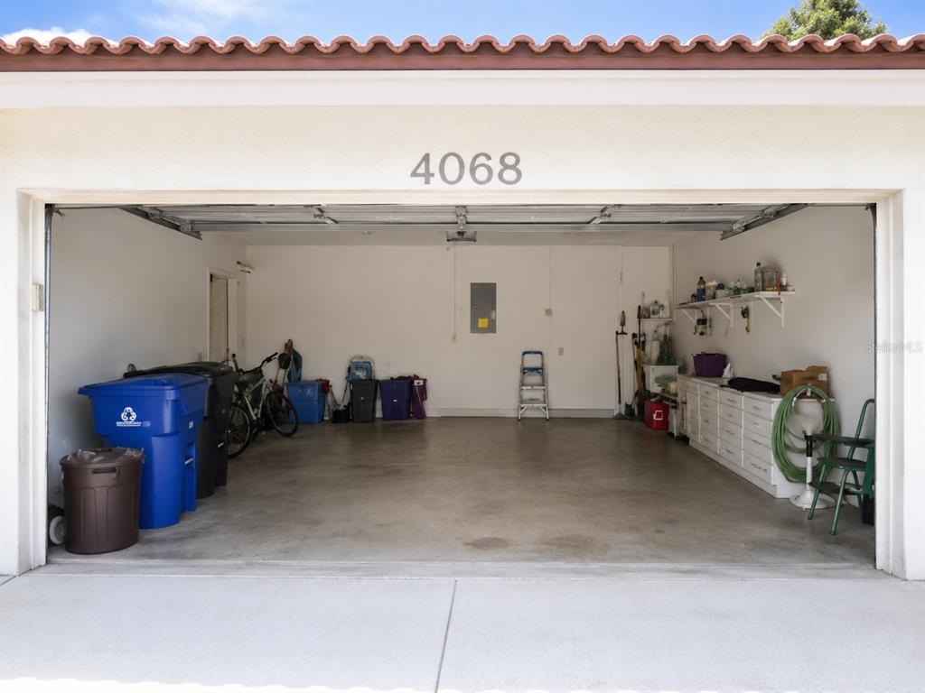 An open garage with a concrete floor, storage cabinets, and various items stored inside — 4068 WILSHIRE CIRCLE E UNIT 145, SARASOTA, FL