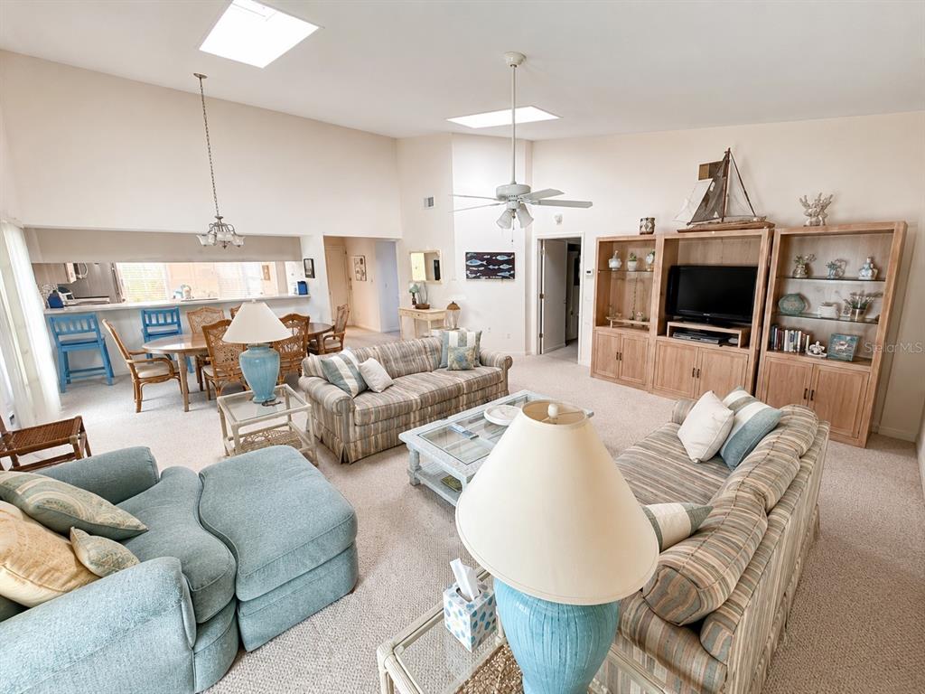 A living room with vaulted ceilings, skylights, two sofas, and an adjacent dining area — 4068 WILSHIRE CIRCLE E UNIT 145, SARASOTA, FL