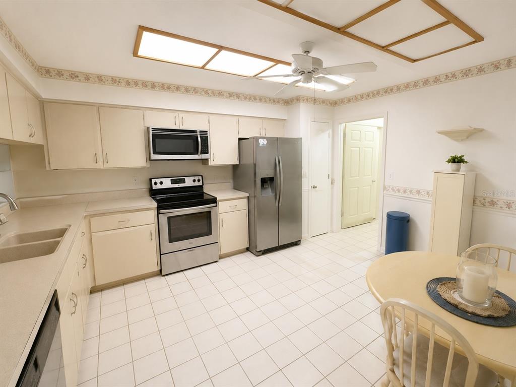A kitchen with off-white cabinets, stainless steel appliances, tile flooring, and a dining table — 4068 WILSHIRE CIRCLE E UNIT 145, SARASOTA, FL