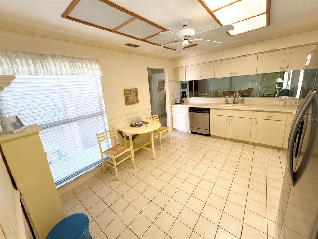 A kitchen features white cabinets, a tiled floor, a small dining table, and a ceiling fan — 4068 WILSHIRE CIRCLE E UNIT 145, SARASOTA, FL