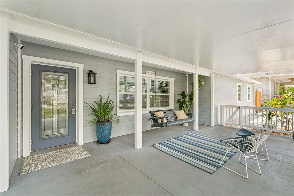 A covered porch features a gray front door, a hanging bench, and outdoor seating — 302 W COMANCHE AVENUE, TAMPA, FL