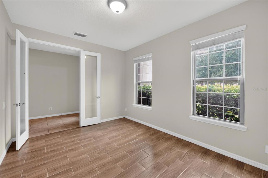 An empty room with wood-look tile flooring, light walls, and white French doors — 2130 LANDSIDE DRIVE, VALRICO, FL