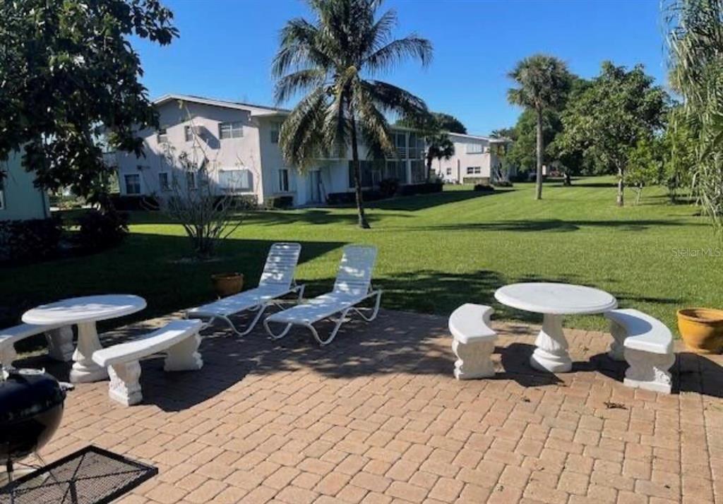 A paved patio features white stone benches, tables, and lounge chairs overlooking a grassy lawn — 66 EASTHAMPTON UNIT C, WEST PALM BEACH, FL